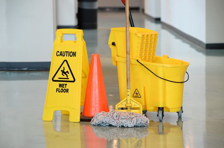 A yellow “Caution Wet Floor” sign, orange traffic cone, yellow mop bucket with wringer, and mop on a shiny indoor floor.