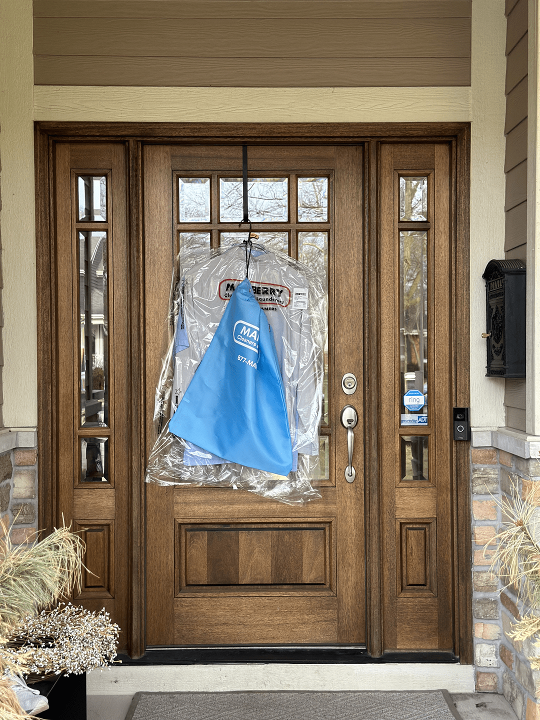 A dry cleaning garment and a blue cloth bag are hanging from the handle of a wooden front door with glass panels.