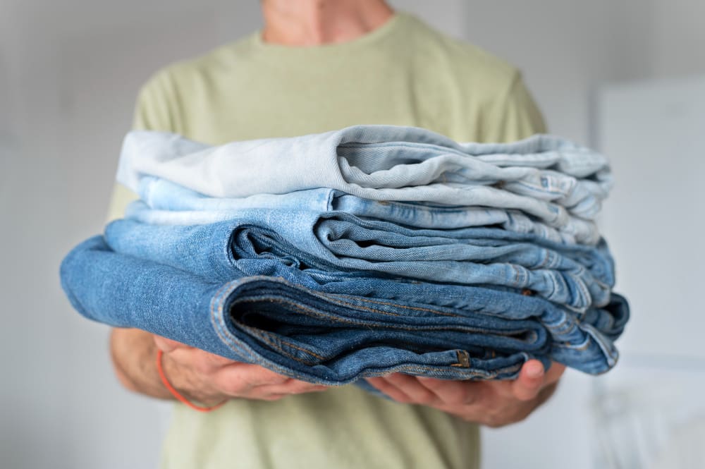 A person holding a stack of four folded denim jeans in varying shades of blue.
