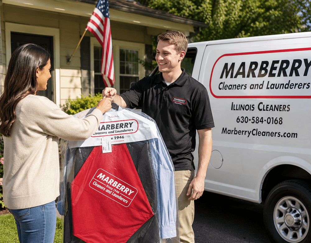 A man hands cleaned clothes in plastic covers to a woman outside her home, standing next to a Marberry Cleaners van.